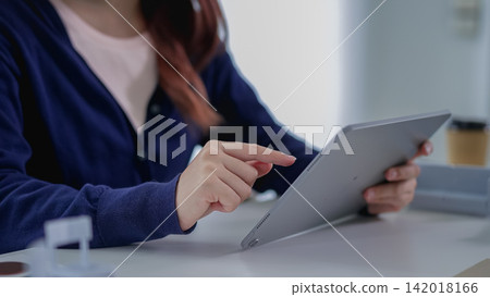 Young Asian professional woman pointing at digital tablet screen while working at modern office desk Young Asian professional woman pointing at digital tablet screen while working at modern office desk 142018166