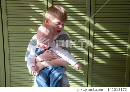 Older brother holds crying baby sibling in his arms and tries to comfort him at home. Brotherhood, sibling care, caregiving, protection, responsibility, emotional support, childhood, family bond Older brother holds crying baby sibling in his arms and tries to comfort him at home. Brotherhood, sibling care, caregiving, protection, responsibility, emotional support, childhood, family bond 142018172