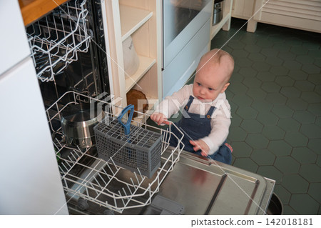 Baby explores open dishwasher and reaches toward lower rack in home kitchen. Early childhood, curiosity, household safety, child development, exploration, learning, domestic life, everyday family Baby explores open dishwasher and reaches toward lower rack in home kitchen. Early childhood, curiosity, household safety, child development, exploration, learning, domestic life, everyday family 142018181
