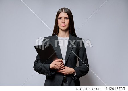 Serious businesswoman holding laptop isolated on grey studio background Serious businesswoman holding laptop isolated on grey studio background 142018735