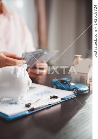 Piggy bank, blue car, wooden house, cash, and financial report show household budgeting, saving for major purchases, asset building, money management, and long-term financial goals. 142019724