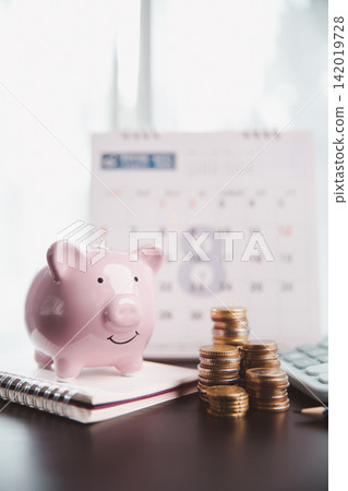 Pink piggy bank on a notebook beside stacked coins, calculator, and blurred calendar, symbolizing monthly savings, household budgeting, financial planning, deadlines, and future security. Pink piggy bank on a notebook beside stacked coins, calculator, and blurred calendar, symbolizing monthly savings, household budgeting, financial planning, deadlines, and future security. 142019728