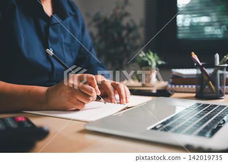 Business professional writing budget notes beside a laptop and calculator, representing accounting, expense calculation, financial planning, bookkeeping, and business finance management. Business professional writing budget notes beside a laptop and calculator, representing accounting, expense calculation, financial planning, bookkeeping, and business finance management. 142019735