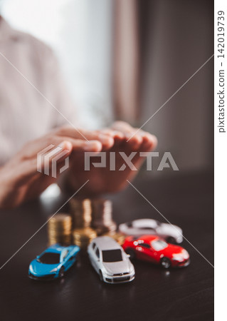 Protective hands hover above multiple car models and coin stacks, illustrating fleet insurance, asset protection, risk management, financial planning, business mobility, Protective hands hover above multiple car models and coin stacks, illustrating fleet insurance, asset protection, risk management, financial planning, business mobility, 142019739