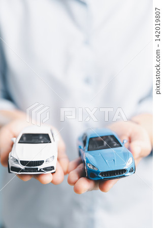 White and blue toy cars held in both hands represent vehicle comparison, purchase decision, financing options, and choosing between car models or ownership plans. White and blue toy cars held in both hands represent vehicle comparison, purchase decision, financing options, and choosing between car models or ownership plans. 142019807