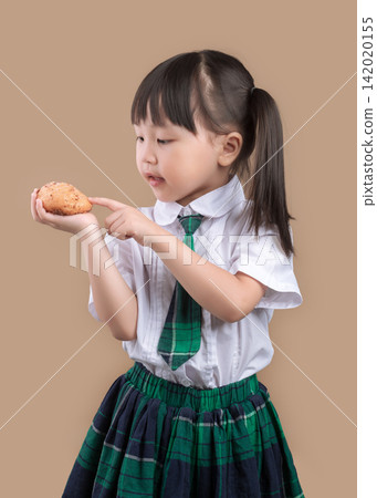 Hungry schoolgirl with pigtails taking a big bite of a delicious bread. Hungry schoolgirl with pigtails taking a big bite of a delicious bread. 142020155