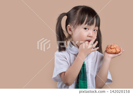 Hungry schoolgirl with pigtails taking a big bite of a delicious bread. Hungry schoolgirl with pigtails taking a big bite of a delicious bread. 142020158