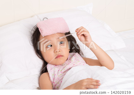 Sick little girl lying in bed and looking anxiously at a glass thermometer in her hand. Sick little girl lying in bed and looking anxiously at a glass thermometer in her hand. 142020159