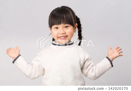 Cheerful little girl in white winter sweater spreading arms with an open friendly smile. Cheerful little girl in white winter sweater spreading arms with an open friendly smile. 142020170