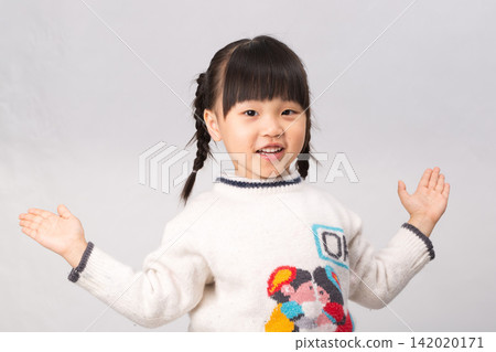 Cheerful little girl in white winter sweater spreading arms with an open friendly smile. Cheerful little girl in white winter sweater spreading arms with an open friendly smile. 142020171