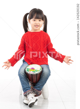 Smiling East Asian girl waving hand while playing an African djembe drum. Smiling East Asian girl waving hand while playing an African djembe drum. 142020192