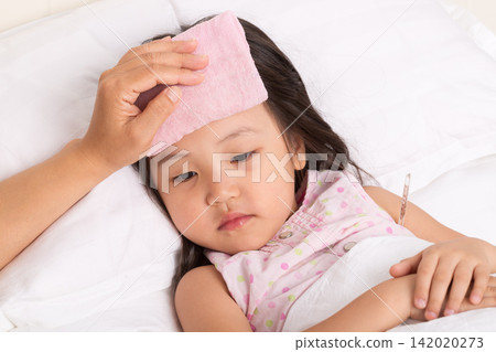 The sick little girl lay peacefully asleep in bed, a pink, damp towel on her forehead. The sick little girl lay peacefully asleep in bed, a pink, damp towel on her forehead. 142020273