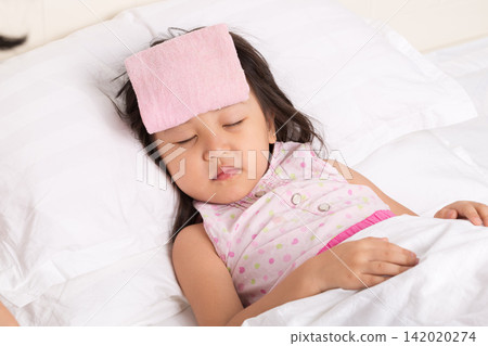 The sick little girl lay peacefully asleep in bed, a pink, damp towel on her forehead. 142020274