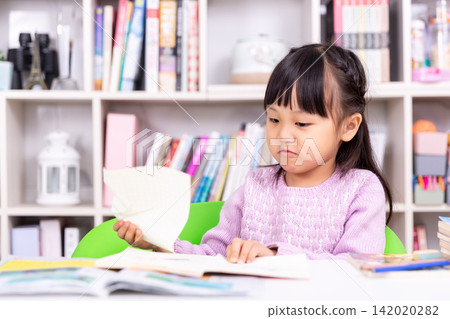 Focused little schoolgirl concentrating on writing or drawing in her notebook at desk. Focused little schoolgirl concentrating on writing or drawing in her notebook at desk. 142020282