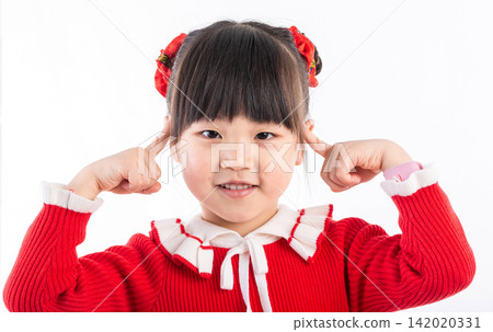 Cute Asian preschool girl in red sweater pointing at her ears with fingers smiling at camera. 142020331