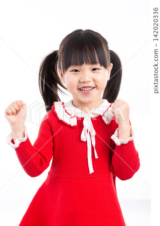 Joyful little schoolgirl in a festive red dress raising her fists and celebrating happily. 142020336