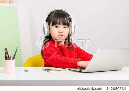 Diligent Asian schoolgirl typing on laptop keyboard during online elementary class. 142020384