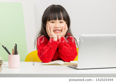 Lovely Asian child smiling at camera while turning pages of her textbook. Lovely Asian child smiling at camera while turning pages of her textbook. 142020394
