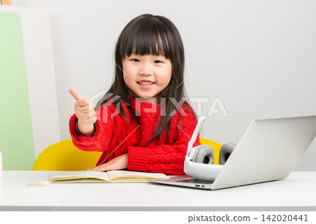 Positive little Asian girl showing thumbs up gesture during an e-learning session. Positive little Asian girl showing thumbs up gesture during an e-learning session. 142020441