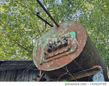 Old industrial hot water tank mounted above a small utility building showing vintage engineering and weathered metal equipment Old industrial hot water tank mounted above a small utility building showing vintage engineering and weathered metal equipment 142020789