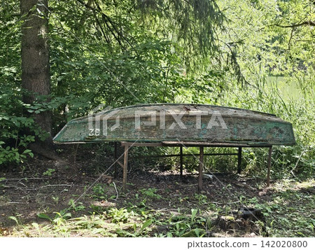 Old overturned wooden fishing boat abandoned on a quiet riverbank surrounded by tall grass and wild nature Old overturned wooden fishing boat abandoned on a quiet riverbank surrounded by tall grass and wild nature 142020800
