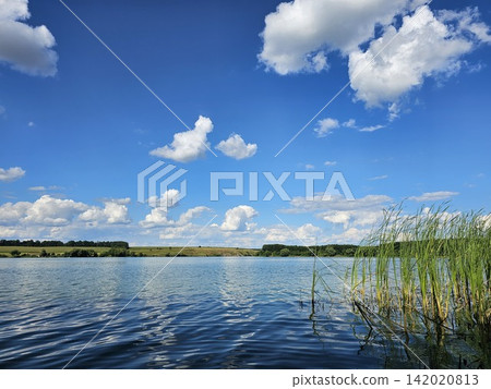 Calm Southern Bug River with green reeds and blue summer sky creating a peaceful natural landscape in warm sunny weather Calm Southern Bug River with green reeds and blue summer sky creating a peaceful natural landscape in warm sunny weather 142020813