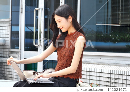 A young woman opens her laptop and works on it on a bench on an outdoor terrace. A young woman opens her laptop and works on it on a bench on an outdoor terrace. 142021671