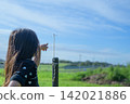A girl's back view as she points to a dragonfly perched on a fence in a pasture in Tohoku | A wide composition reveals a curious childhood. 142021886