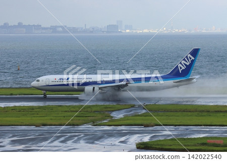 A passenger plane lands on a rainy runway, producing a plume of water from the engine's reverse thrust. A passenger plane lands on a rainy runway, producing a plume of water from the engine's reverse thrust. 142022540