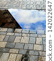 The blue sky and buildings reflected in the puddles on the cobblestones 142022647