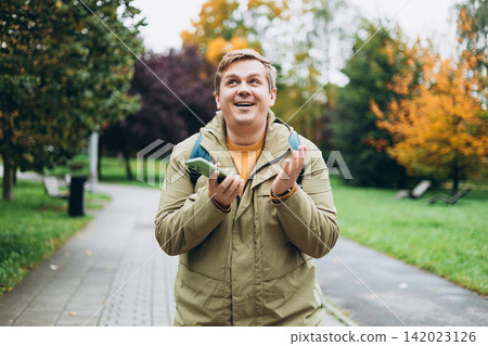 Male using mobile phone app, playing game, shopping online outdoors. Happy man celebrating victory in lottery in the park. Amazed hipster wondered with win in online auction betting on website Male using mobile phone app, playing game, shopping online outdoors. Happy man celebrating victory in lottery in the park. Amazed hipster wondered with win in online auction betting on website 142023126