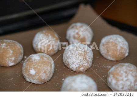 Raw almond cookie dough balls coated with powdered sugar rest on baking paper before baking. Home baking, dessert preparation, confectionery, handmade pastry, recipe, baking process, homemade food Raw almond cookie dough balls coated with powdered sugar rest on baking paper before baking. Home baking, dessert preparation, confectionery, handmade pastry, recipe, baking process, homemade food 142023213