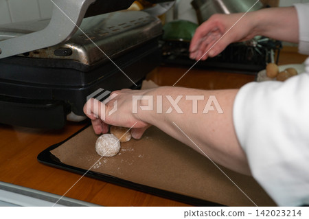 Woman places powdered almond cookie dough balls on baking tray before baking in home kitchen. Home baking, dessert preparation, handmade pastry, confectionery, cooking process, homemade food 142023214