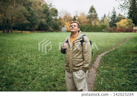 Happy 30s blonde man with backpack standing in the countryside. Traveler. Autumn time. Positive handsome blonde male standing outdoor Happy 30s blonde man with backpack standing in the countryside. Traveler. Autumn time. Positive handsome blonde male standing outdoor 142023284