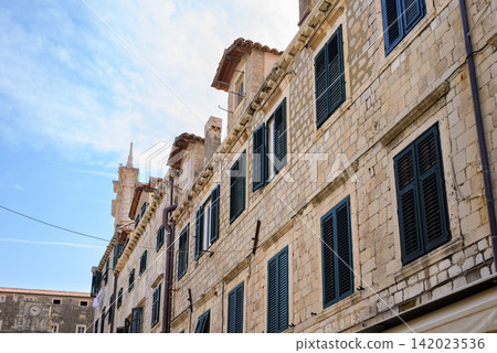 A historic stone multi-story building in a European city facade, featuring dark painted shutters and clean masonry windows A historic stone multi-story building in a European city facade, featuring dark painted shutters and clean masonry windows 142023536