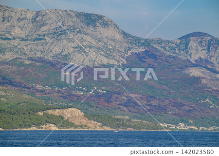A panoramic view of a rugged coastal landscape with a massive rocky mountain range rising sharply from the sea A panoramic view of a rugged coastal landscape with a massive rocky mountain range rising sharply from the sea 142023580