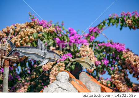 A vibrant outdoor photograph featuring a colorful metal sculpture of a shark and fish against a backdrop of blooming flowers and clear sky A vibrant outdoor photograph featuring a colorful metal sculpture of a shark and fish against a backdrop of blooming flowers and clear sky 142023589