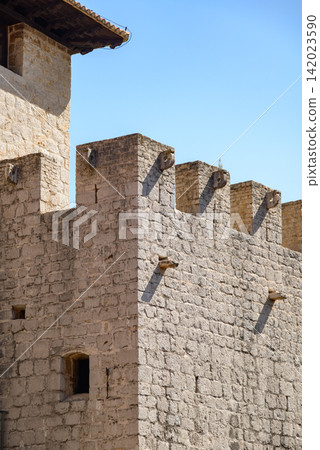 A detailed high-angle photograph of an ancient stone fortress wall under a clear blue sky A detailed high-angle photograph of an ancient stone fortress wall under a clear blue sky 142023590