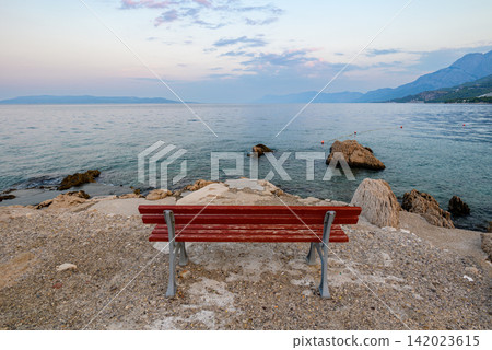 A solitary wooden bench amidst a serene coastal landscape with gentle waves and distant mountains A solitary wooden bench amidst a serene coastal landscape with gentle waves and distant mountains 142023615