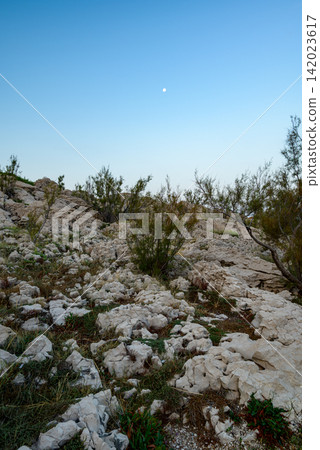 A rugged, rocky landscape under a clear sky with sparse vegetation and a soft blue sky gradient A rugged, rocky landscape under a clear sky with sparse vegetation and a soft blue sky gradient 142023617