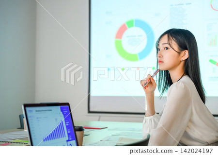 A woman listening to a presentation focuses on the graph on the projector. A woman listening to a presentation focuses on the graph on the projector. 142024197
