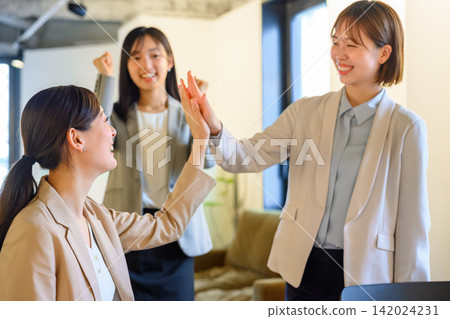 Women in the business team high-five each other in celebration at the office. Women in the business team high-five each other in celebration at the office. 142024231