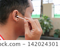 Man gently cleans ear with cotton swab. Focused expression suggests care and hygiene. Outdoor setting with soft natural light. Ideal for health, wellness, or personal care content 142024301