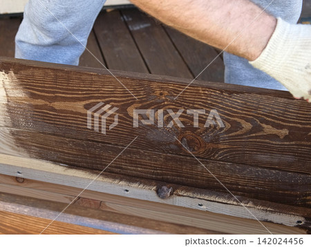 Brown oil for protection of wood by staining. Painting fence for protecting and pests. Woodworker applying finish to pine board box. Repairman varnishing with brush wooden fencing wall plank surface. Brown oil for protection of wood by staining. Painting fence for protecting and pests. Woodworker applying finish to pine board box. Repairman varnishing with brush wooden fencing wall plank surface. 142024456
