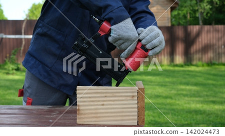 Cropped Image of Male Carpenter shooting nails on wooden frame outdoor. Industrial Cordless Nail Gun Power Tool. Tools efficient for framing, electrical. Carpenter using Air Nailer on timber. Woodwork Cropped Image of Male Carpenter shooting nails on wooden frame outdoor. Industrial Cordless Nail Gun Power Tool. Tools efficient for framing, electrical. Carpenter using Air Nailer on timber. Woodwork 142024473