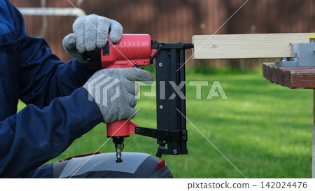 Cropped Image of Male Carpenter shooting nails on wooden frame outdoor. Industrial Cordless Nail Gun Power Tool. Tools efficient for framing, electrical. Carpenter using Air Nailer on timber. Woodwork Cropped Image of Male Carpenter shooting nails on wooden frame outdoor. Industrial Cordless Nail Gun Power Tool. Tools efficient for framing, electrical. Carpenter using Air Nailer on timber. Woodwork 142024476