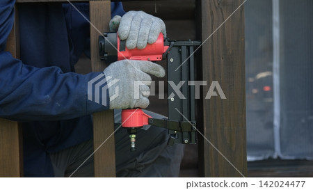 Cropped Image of Male Carpenter shooting nails on wooden frame outdoor. Industrial Cordless Nail Gun Power Tool. Tools efficient for framing, electrical. Carpenter using Air Nailer on timber. Woodwork Cropped Image of Male Carpenter shooting nails on wooden frame outdoor. Industrial Cordless Nail Gun Power Tool. Tools efficient for framing, electrical. Carpenter using Air Nailer on timber. Woodwork 142024477