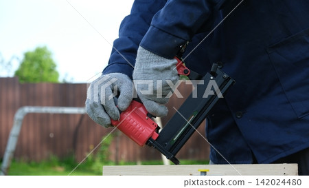 Cropped Image of Male Carpenter shooting nails on wooden frame outdoor. Industrial Cordless Nail Gun Power Tool. Tools efficient for framing, electrical. Carpenter using Air Nailer on timber. Woodwork Cropped Image of Male Carpenter shooting nails on wooden frame outdoor. Industrial Cordless Nail Gun Power Tool. Tools efficient for framing, electrical. Carpenter using Air Nailer on timber. Woodwork 142024480