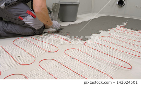 Electric Heating Mat Installing in the Tile Adhesive. Underfloor Dual Core Fiberglass Mesh Mat. Warm Floor Heating System. Warming. Worker Applying Concrete Mortar for Warm Floor. Renovation work. 4K Electric Heating Mat Installing in the Tile Adhesive. Underfloor Dual Core Fiberglass Mesh Mat. Warm Floor Heating System. Warming. Worker Applying Concrete Mortar for Warm Floor. Renovation work. 4K 142024501