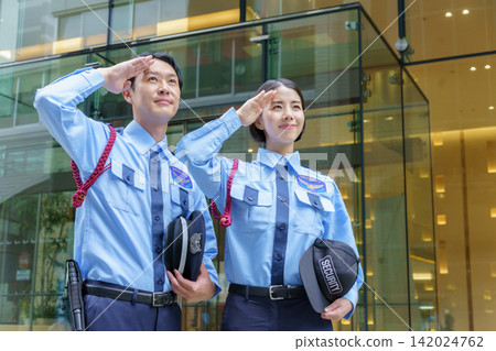 Portrait of a young Japanese male security guard and female security guard standing in front of an office building. Portrait of a young Japanese male security guard and female security guard standing in front of an office building. 142024762